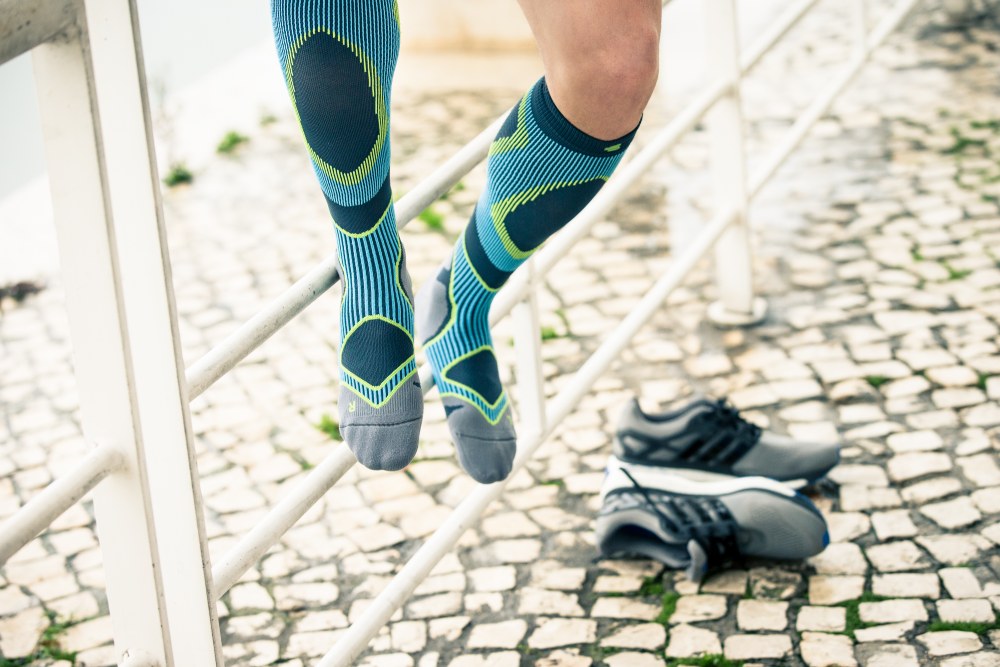 Man with blue and gray running socks sits on a fence and took off the shoes