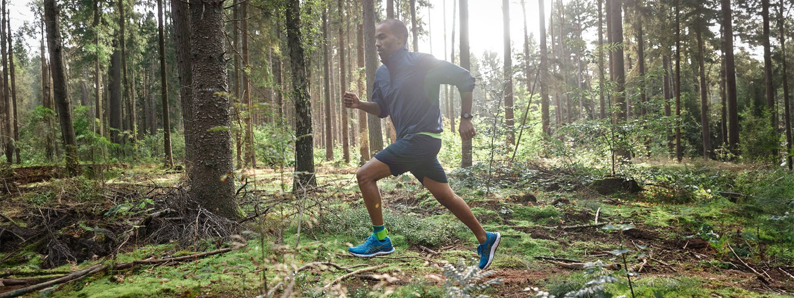 A runner is running through a dense forest against backlight