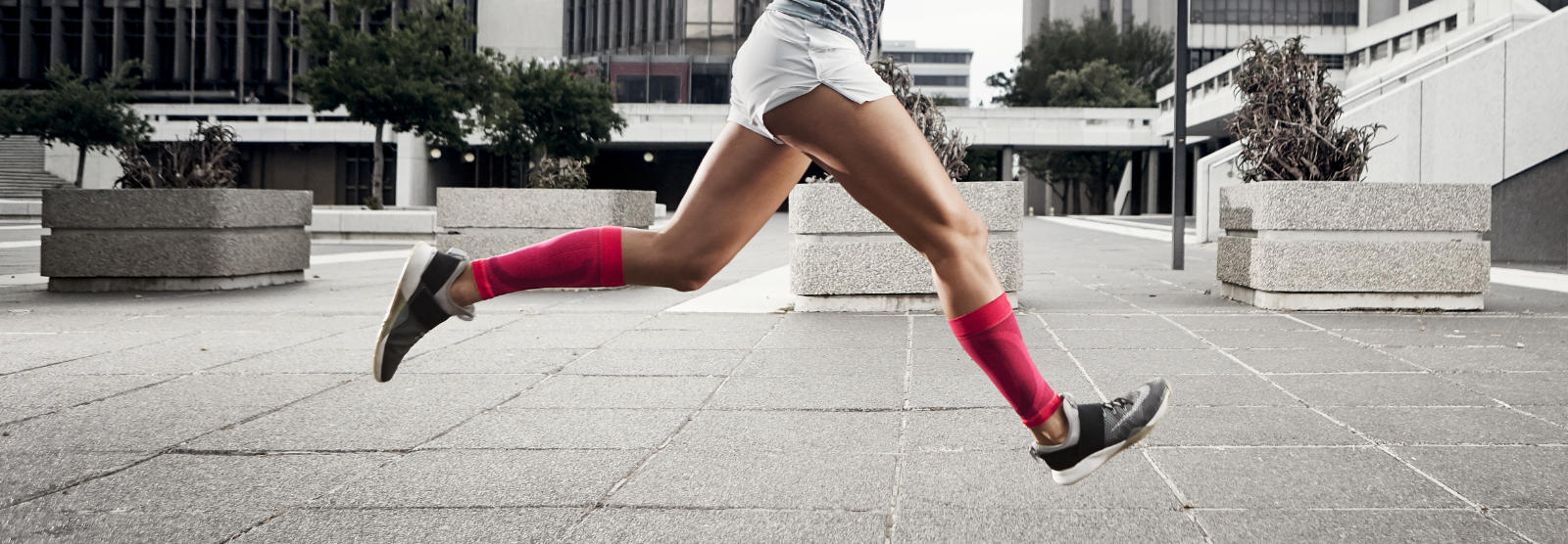 Woman with pink calves runs quickly and with legs in the air through an urban concrete desert