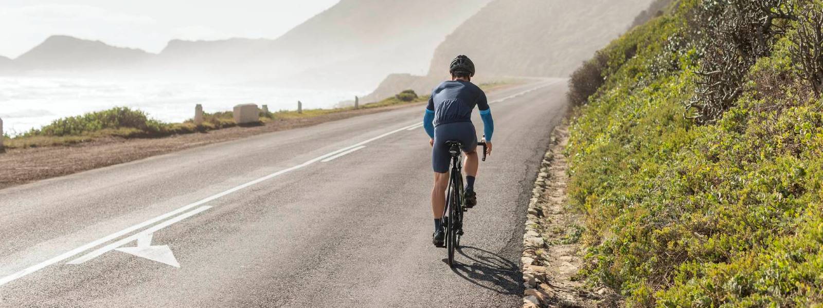 Cyclists wear blue arm sleeves and drives on a street on the slope with a sea view
