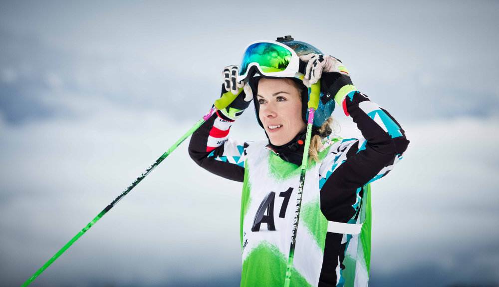 Skir racer Andrea Limbacher in a blue and white-black racing suit addresses her ski glasses with the sticks in her hands