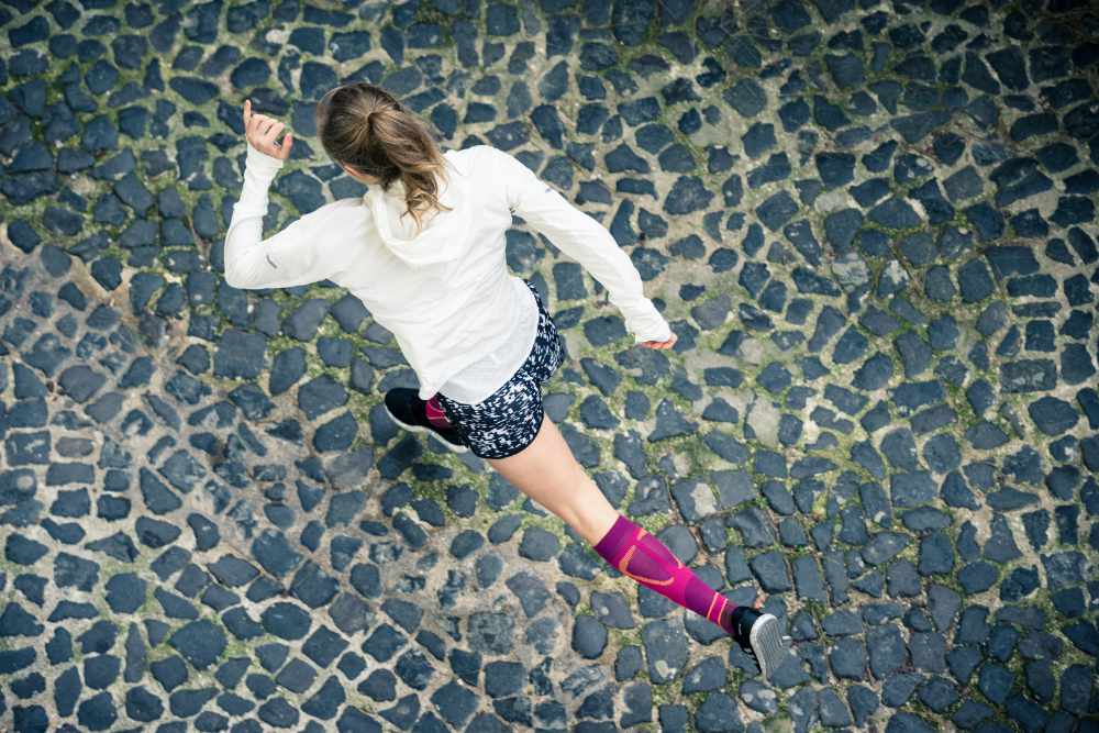 Bird's eye view: runner in a white running jacket and with pink running socks runs over an old town street