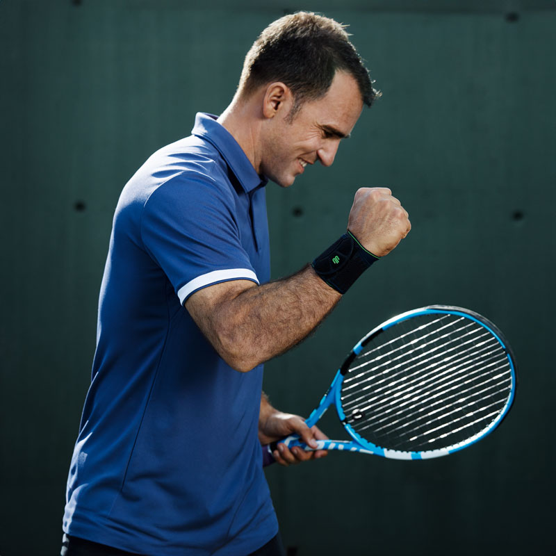 Tennis player with a black wrist bandage lifts his free arm and clumps the fist satisfied
