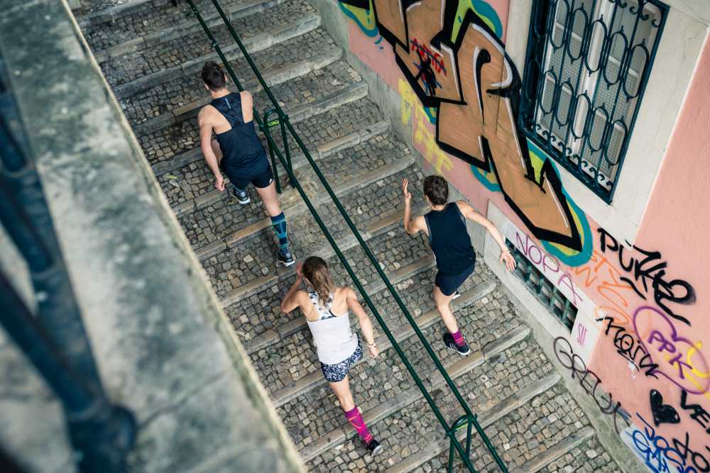 Bird's eye view: A man and two women in running outfits run a staircase in an old town with graffiti on the walls