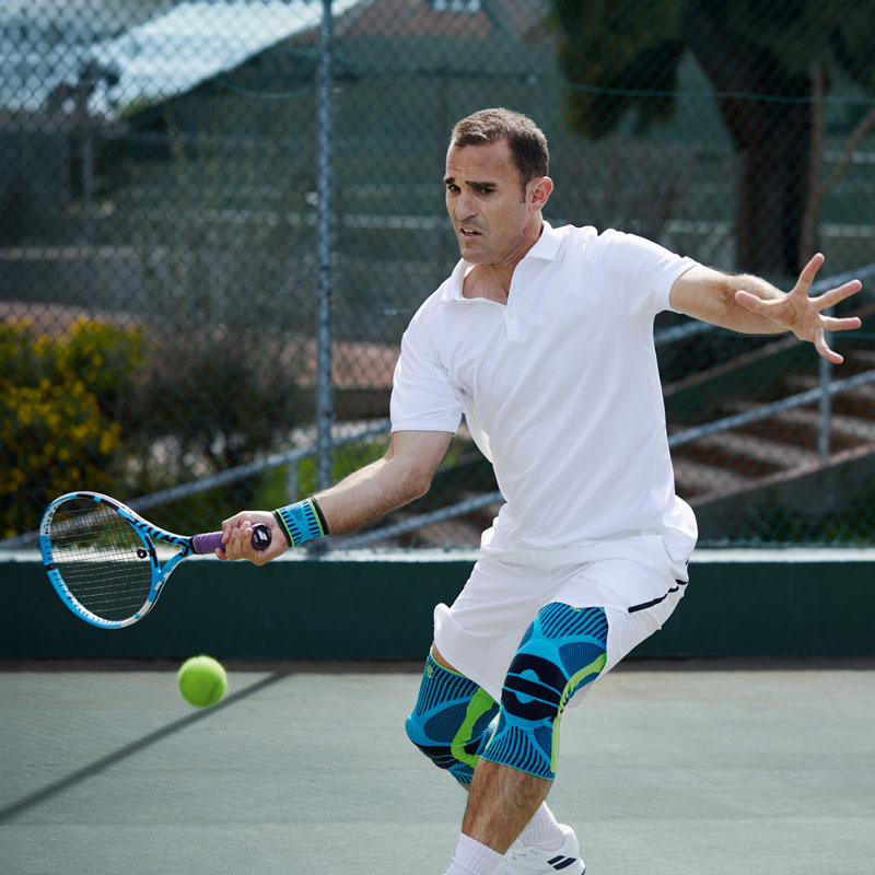 Tennis player with white tennis clothing and knee bars on the forehand stroke on a hard court