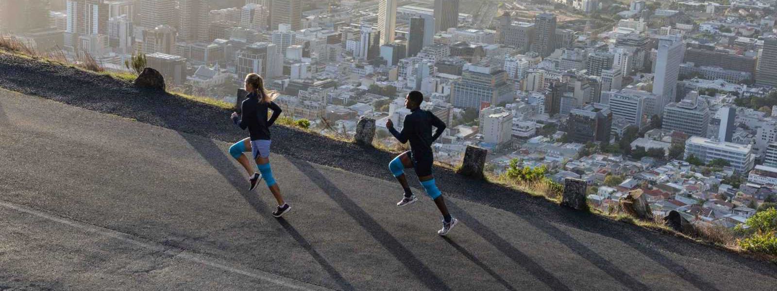 A woman and a man with blue knee bars run up a street above a big city