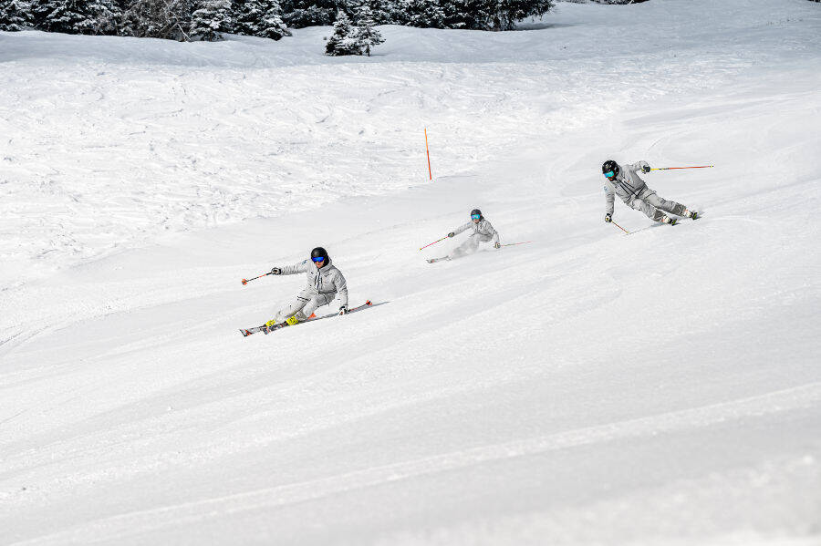 Three skiers dressed in gray gray on the side of a joint descent and in sloping driving positions.