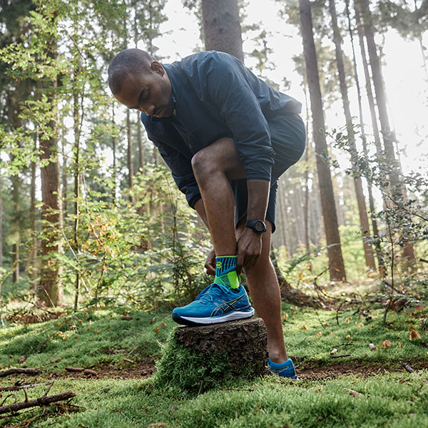 A runner stands in a dense forest adjusting his ankle bandage