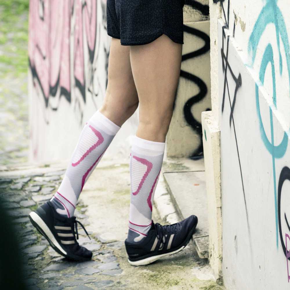 The runner stretches the calves on the door threshold with compression socks in white-pink