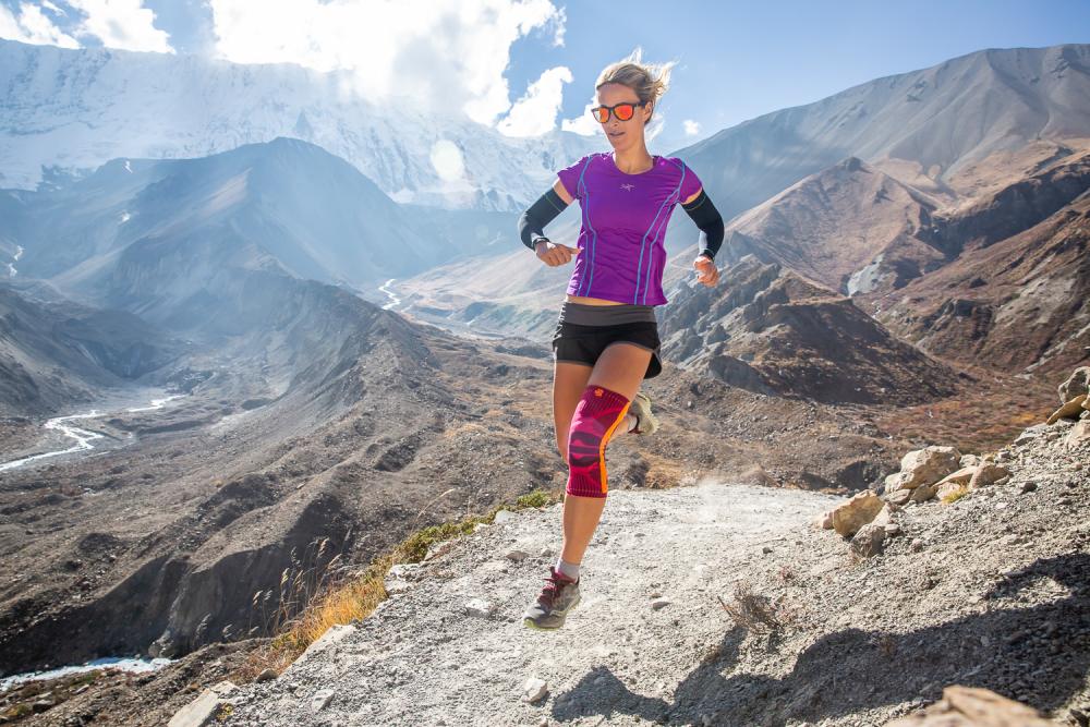 Woman runs through a high mountain landscape and wears a pink kneege