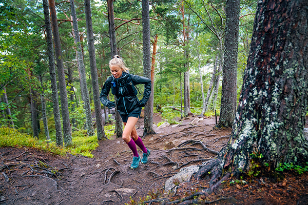 Traill runner with long running socks and training jacket runs up a forest path with many roots