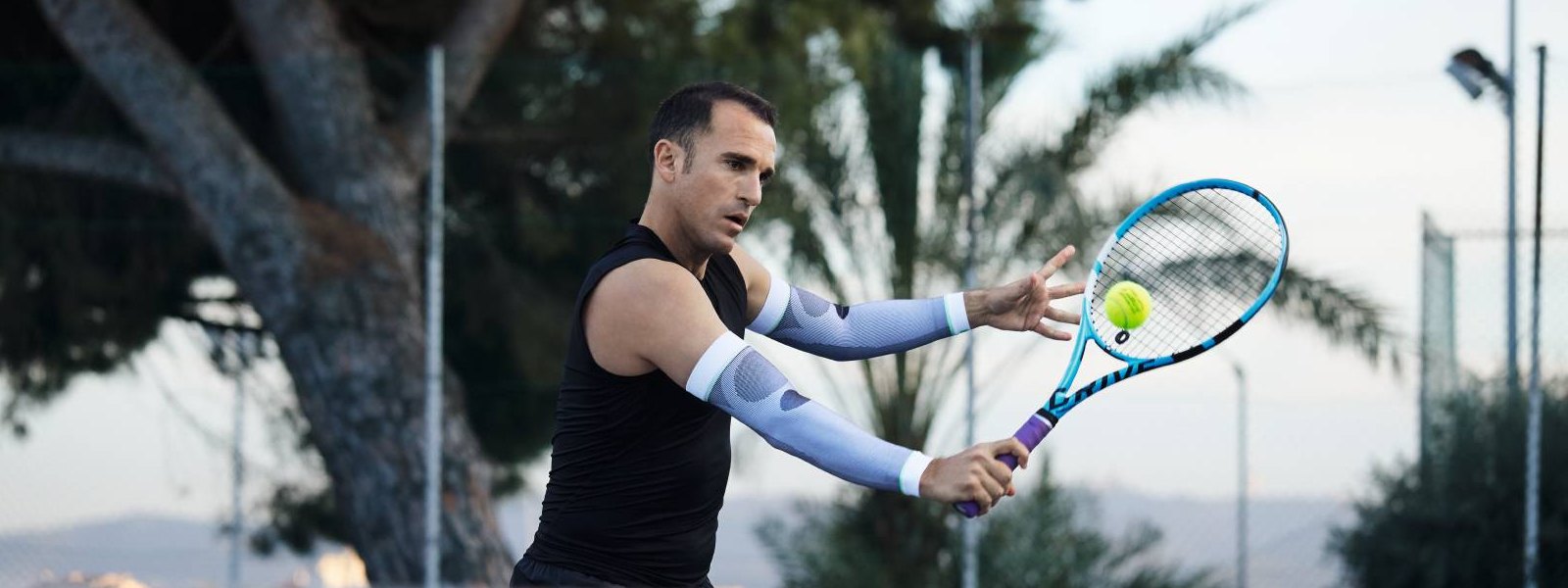 Tennis player with white arm sleeves plays tennis and beats a ball with the backhand