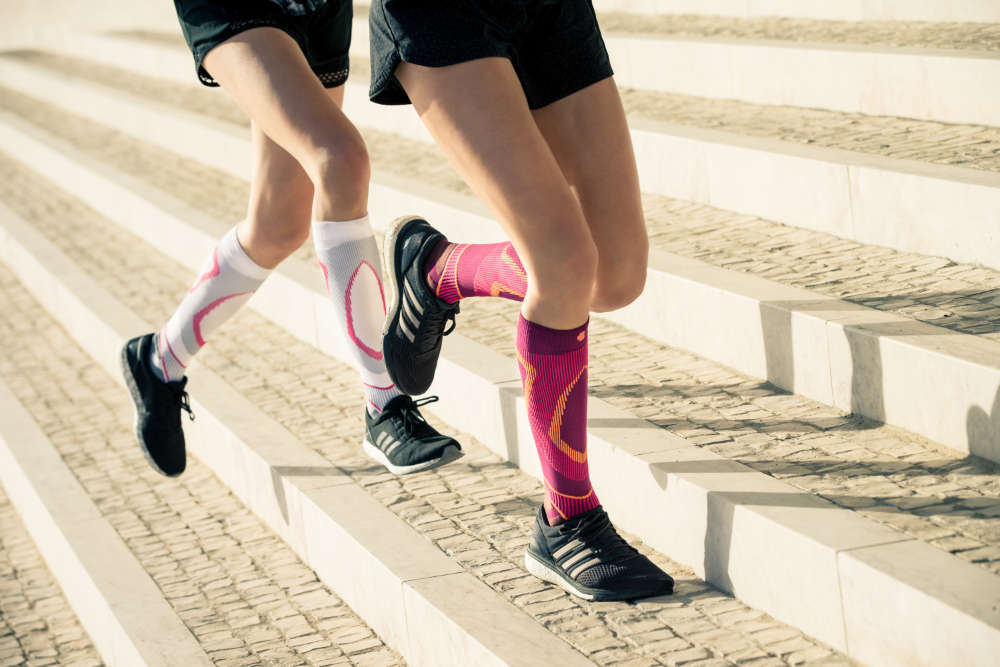 Two thin runners with white and pink running socks run slightly slanted stone steps upwards