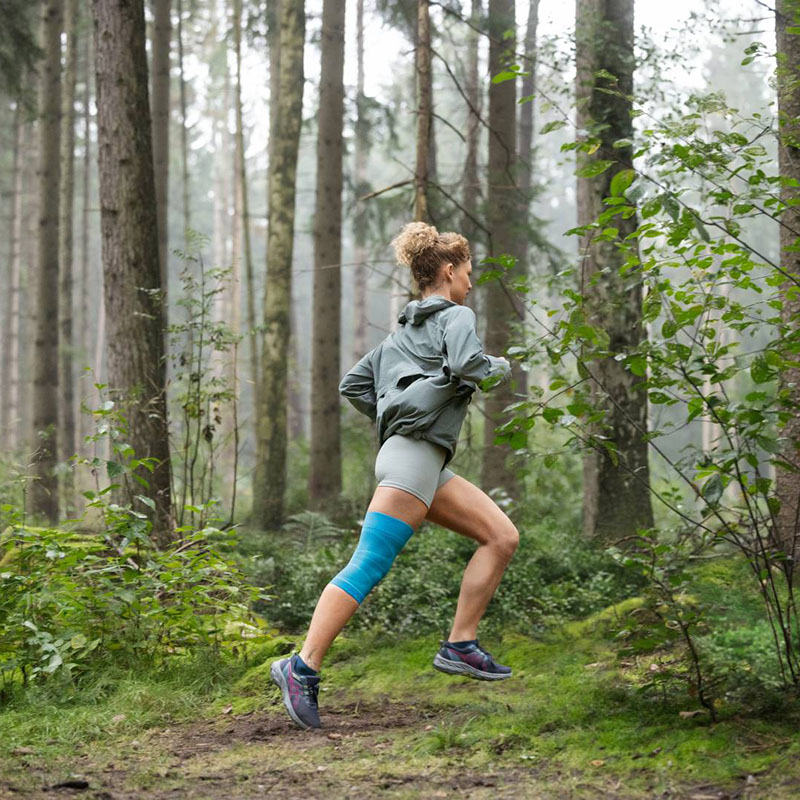 A female runner with a knee bandage is running through a dense forest