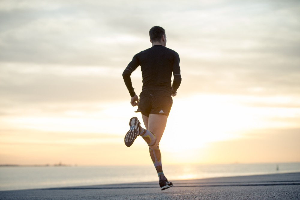 Man with long running socks runs on a promenade towards sunset