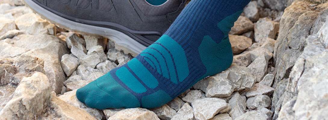 Detailed view of a foot with medium -long Merino - hiking socks on a stony surface - without shoe