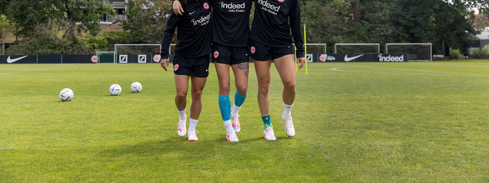Three soccer players with different bandages hug themselves to a lawn