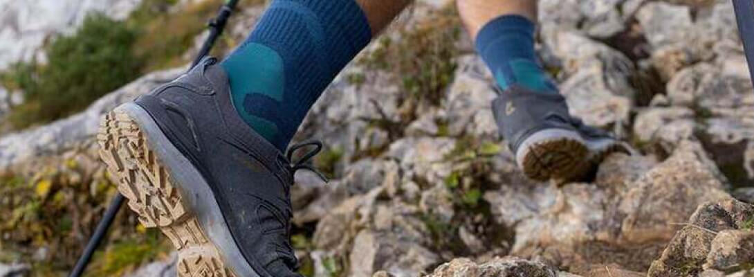 Person goes up a mountain over stones and wears medium -length hiking socks