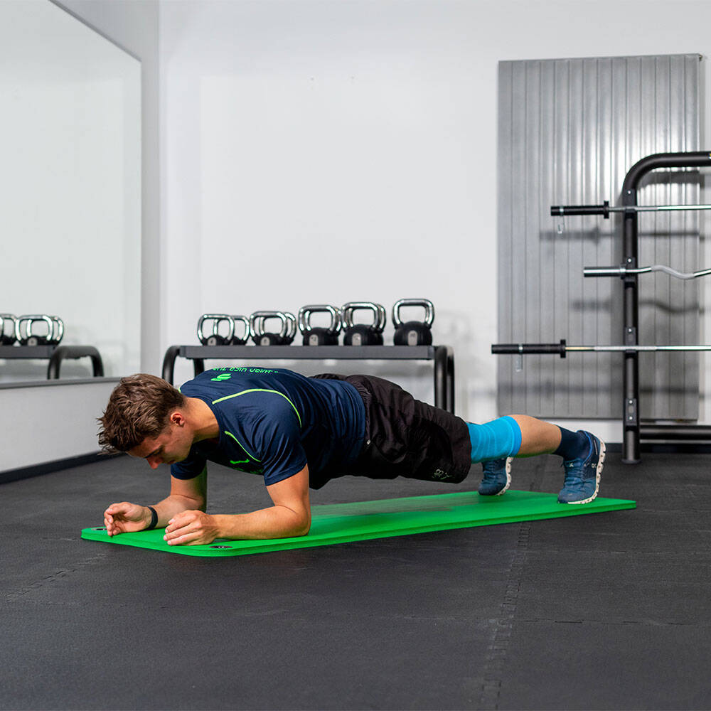 Man in the gym holds a forearm plank on a fitness mat