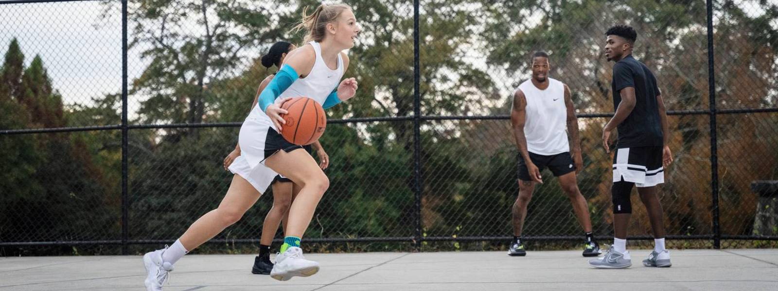 Basketball player dribbles past her opponents on a free space and wears blue arm Sleeves