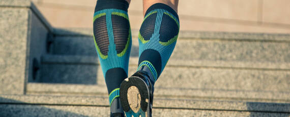 The calf of a runner with gray-blue running socks from behind