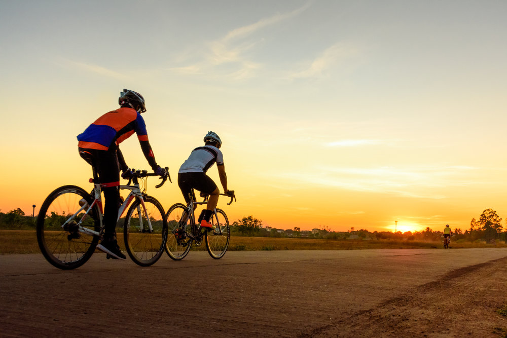 Two racing cyclists drive into the sunset on a flat concrete road