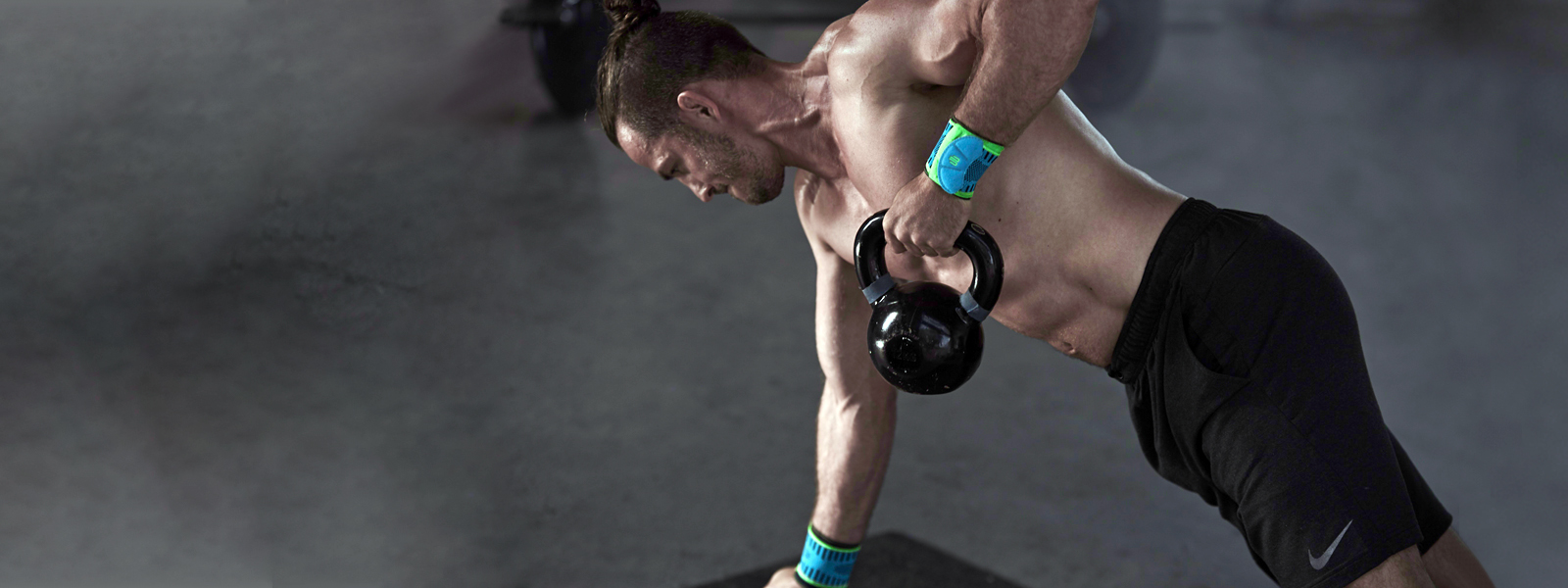 Athletic man with free torso and wrist bandages trains with the kettlebell One hand supports the other pulls up the kettlebell