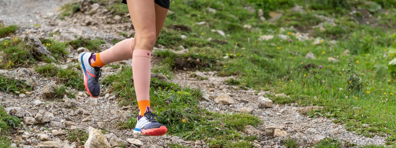 The runner runs down a mountain and wears the Trail Run Socks in the color Peach