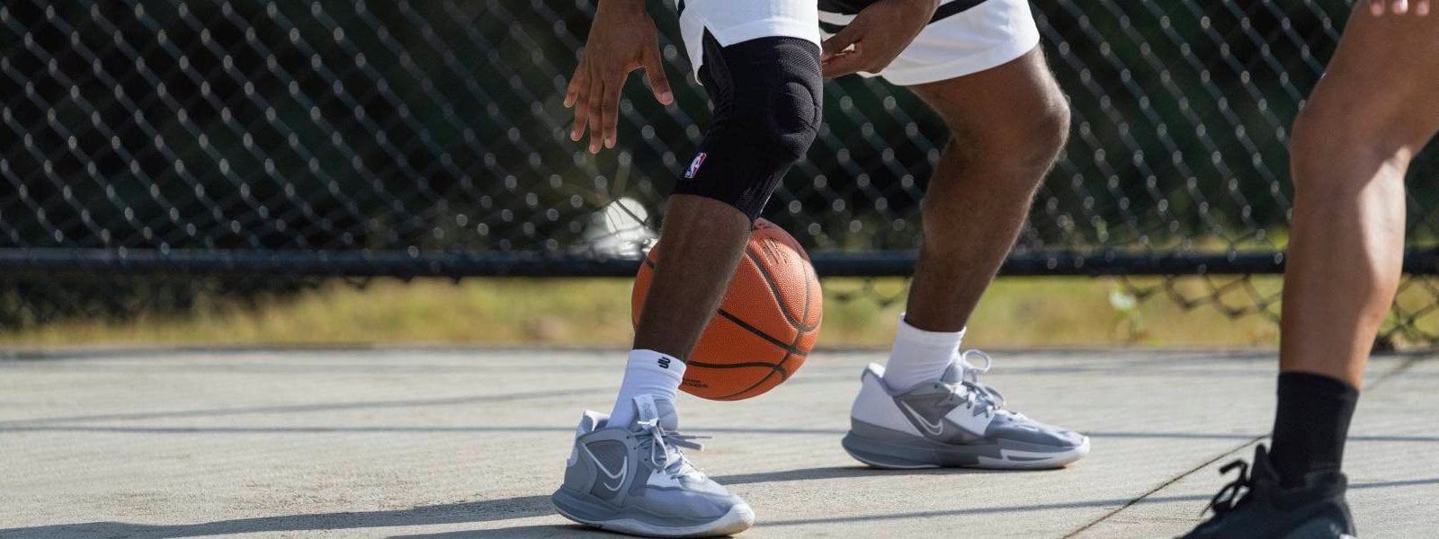 Player dribbles on a streetball court with a basketball and wears a black NBA Knee Support