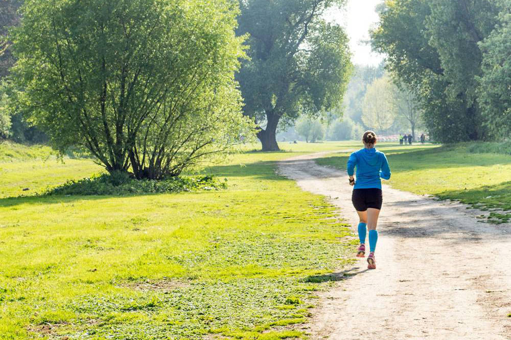 Woman with a blue sweater and blue Waden-Sleeves runs through the park back view