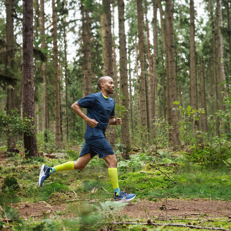 A runner is running quickly through a dense forest wearing compression socks