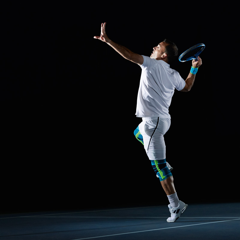 Tennis player in white clothing against a black background on the serve