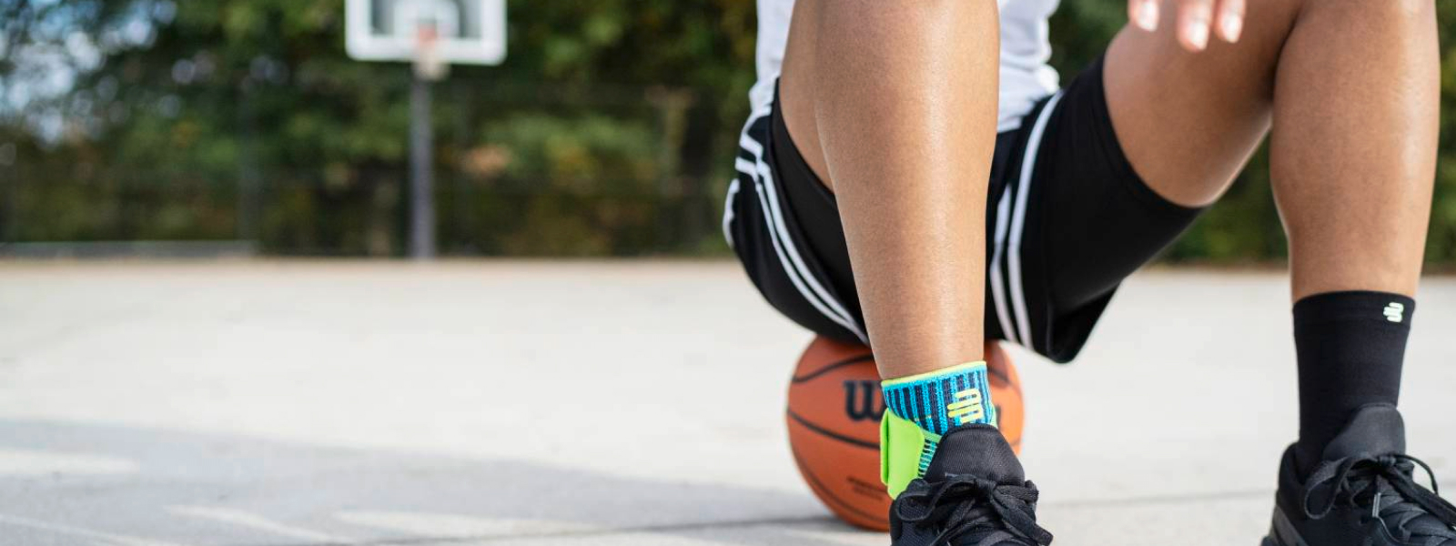 Streetball player with foot bandage sits on a basketball on a street court field