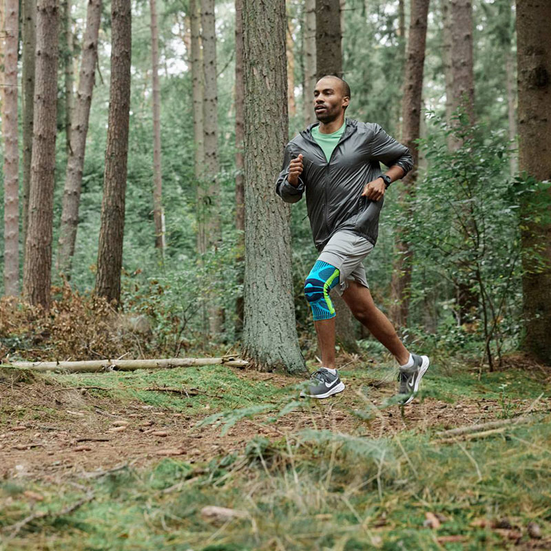 A runner dynamically runs through the forest wearing a knee bandage