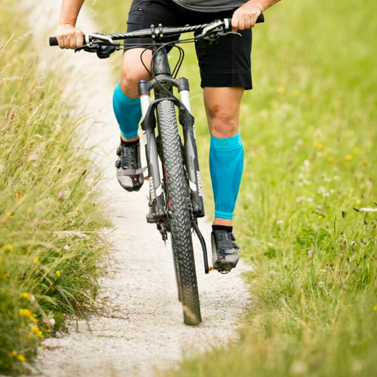Frontal recording cyclist wears Waden-Sleeves while driving via a gravel path on the mountain bike