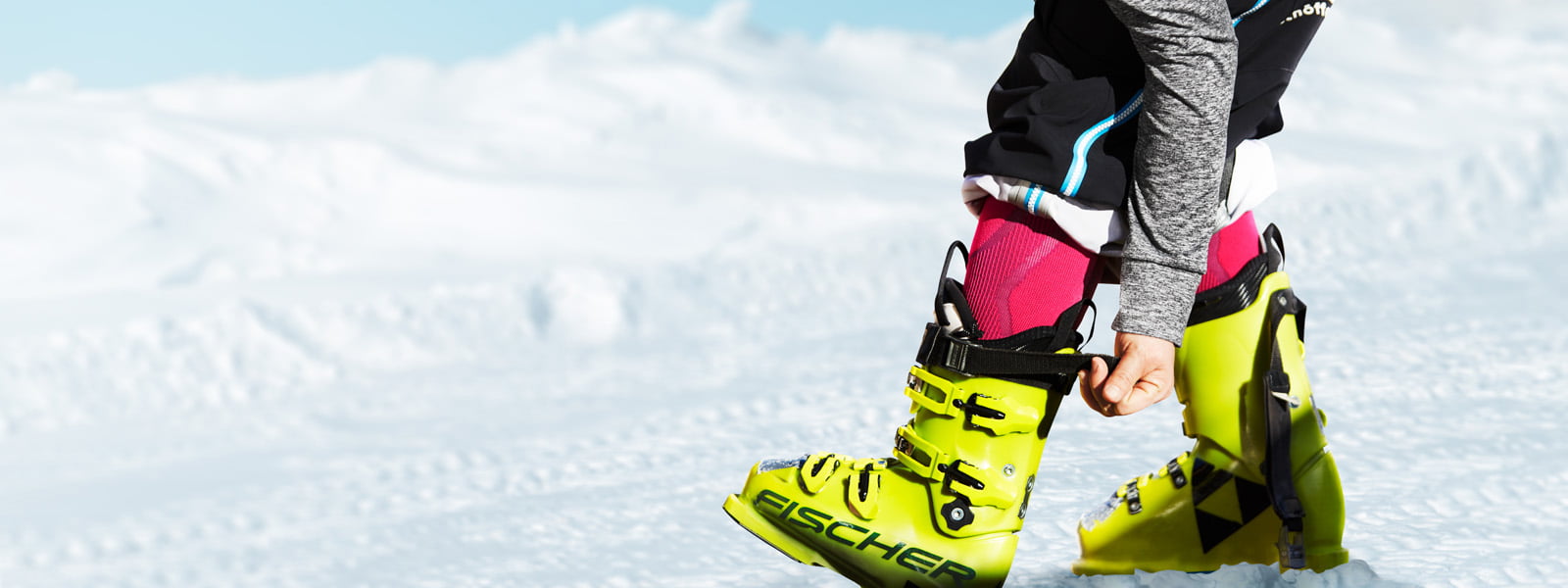 Skiers with pink ski socks and gray sleeves pull the belt firmly in the background of his yellow ski boot in the background