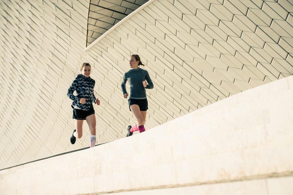Two runners run next to a modern wall in the urban environment and talk