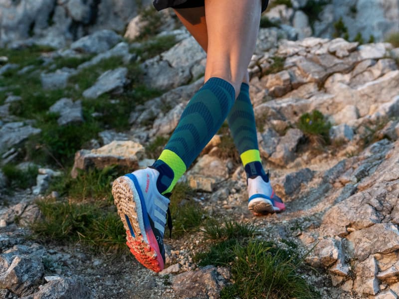The runner runs up stony downhill and wears Trail Run Socks