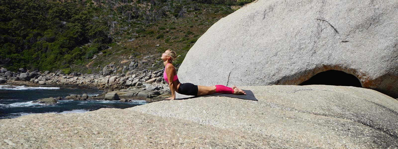 Woman does yoga exercises on a large rock on the water and pink lower leg Sleeves