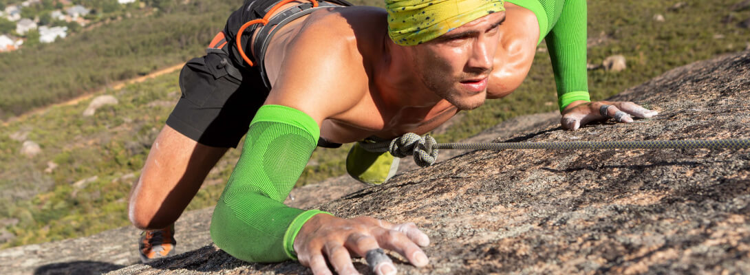 The climber on the rock wears green compression Sleeves for the arm
