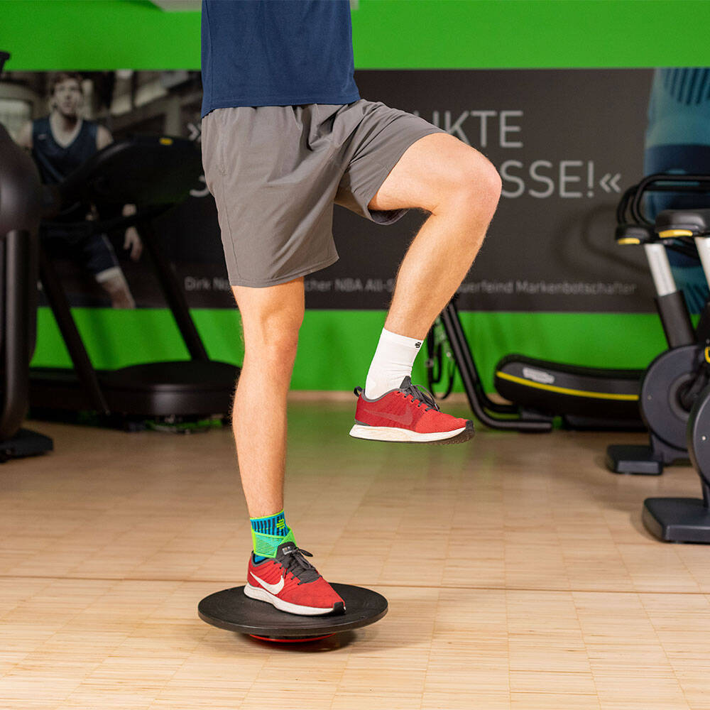 Man in a gym balanced with his right leg on a balance pad and wears an ankle bandage