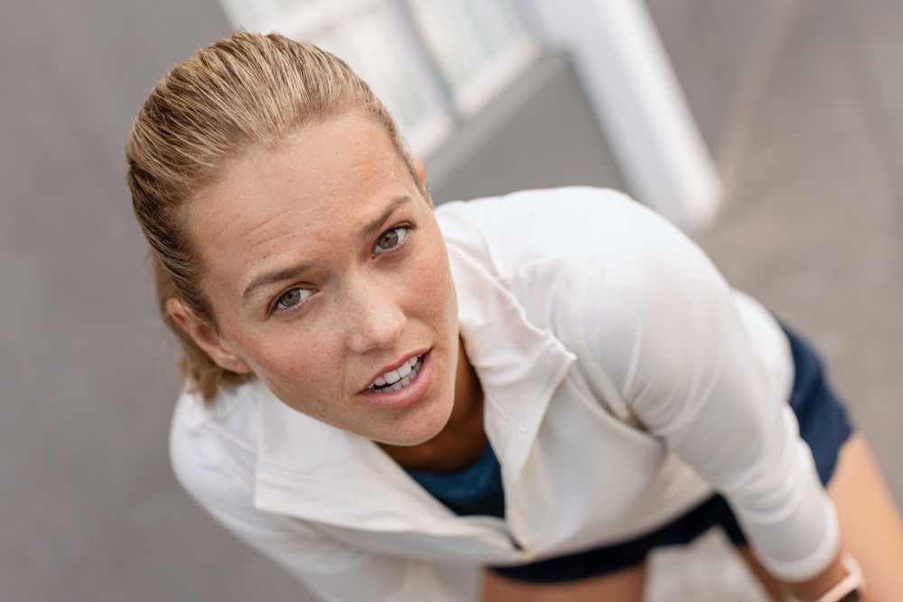 Blonde woman with a white sports sweater looks directly into the camera