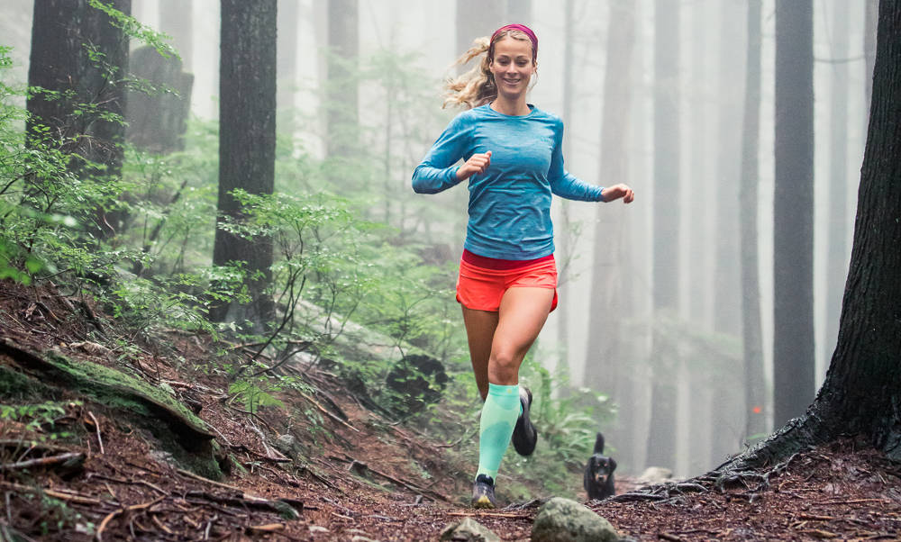 Woman runs in long outdoor socks and with a dog over a forest path