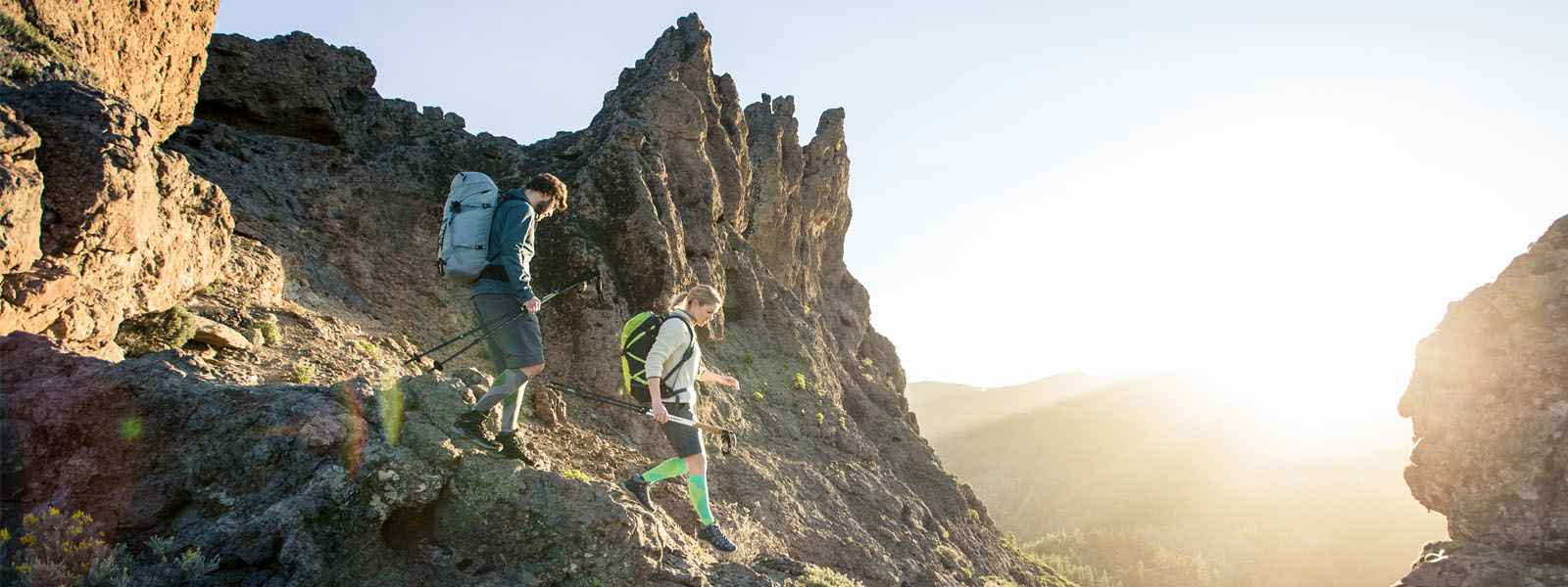Two hikers with long hiking socks go down a steep path on a mountain at dusk
