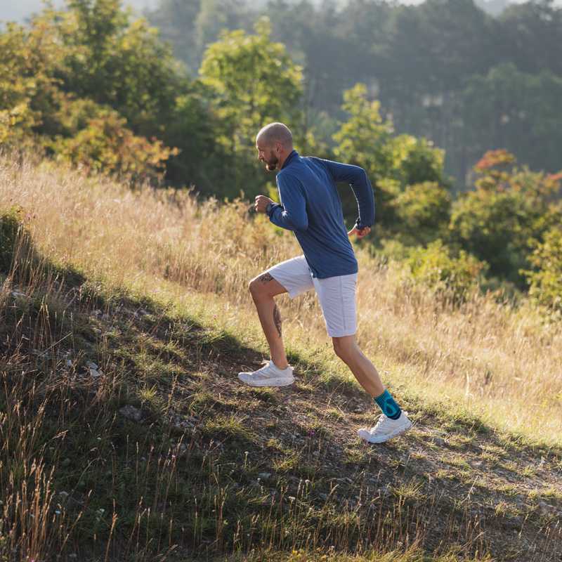 Man runs up a hill with grass with an Achilles tendon bandage on the foot