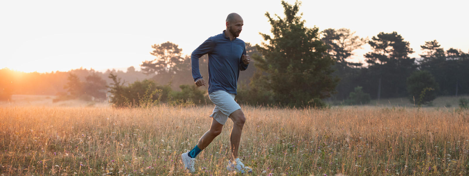 Man with ankle bandage runs at dusk over a meadow with a high grass
