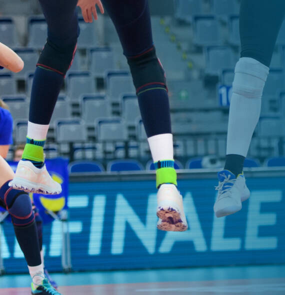 Volleyball player with dark pants white shoes and blue ankle bandages "stands" in the air