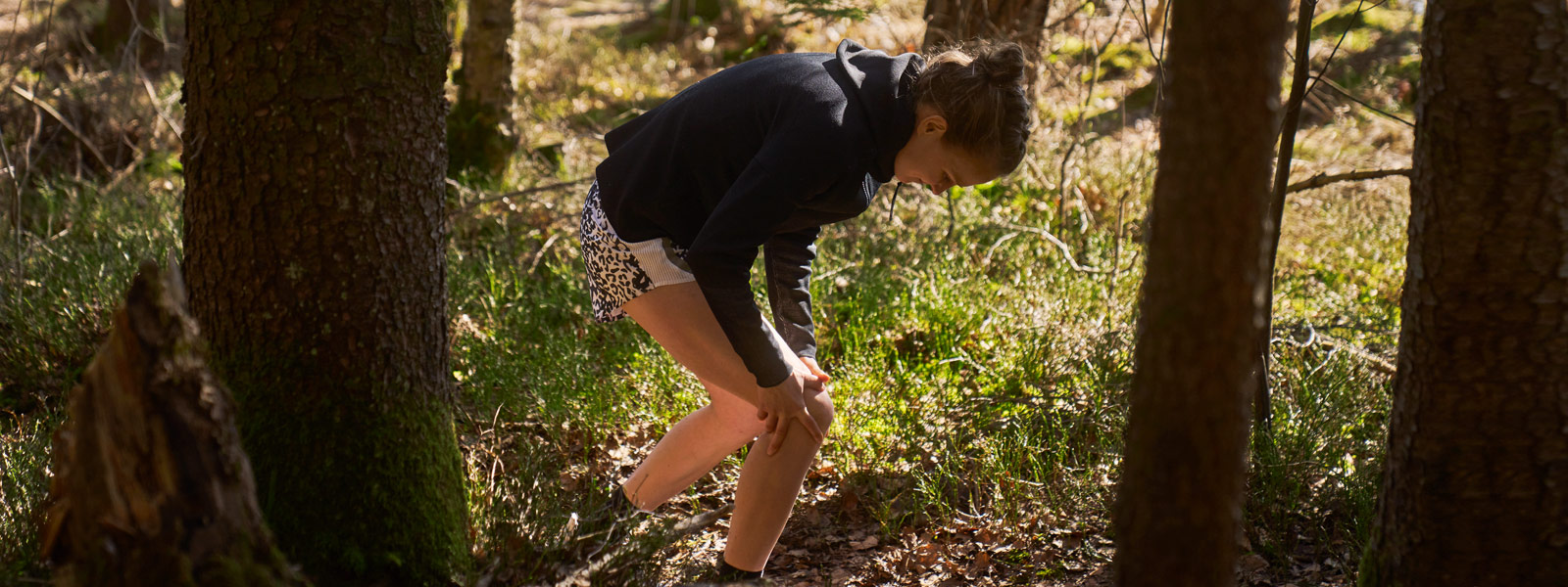 Breaker in dark hoodie grabs her knee standing in the forest between trees