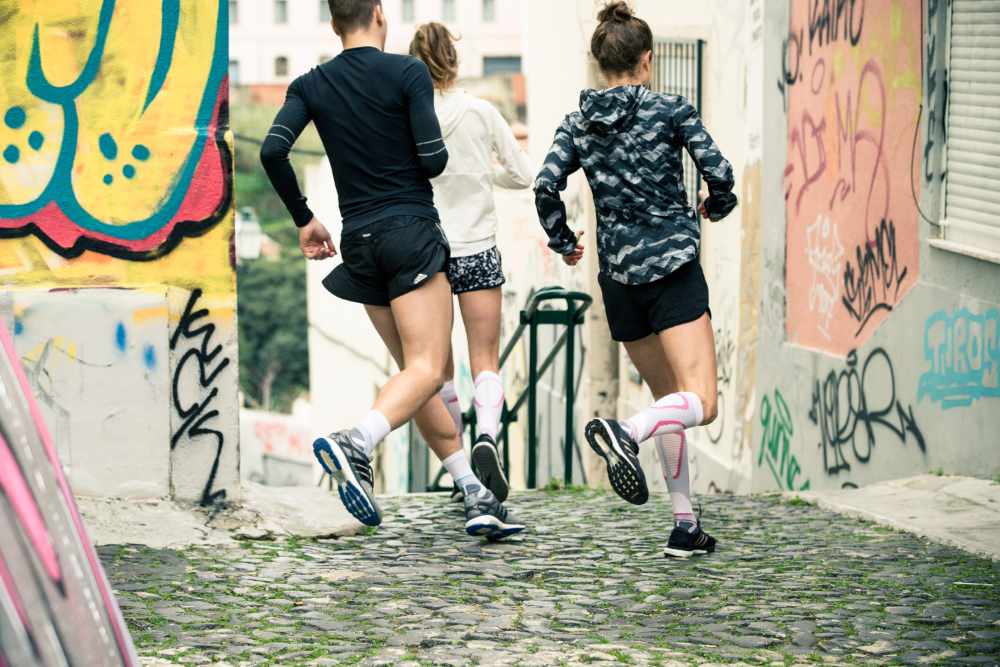 Group of three runners runs around one corner in an old town with graffiti on the walls on a staircase