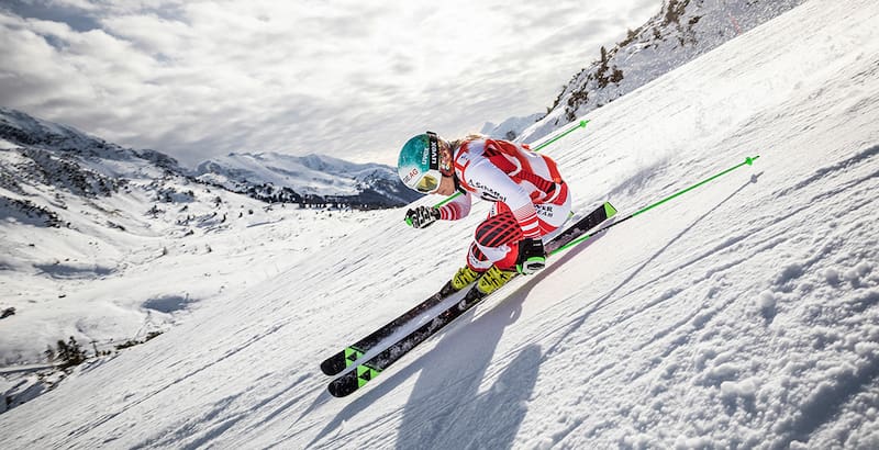Ski driver in a red and white racing suit in an extreme incline on the departure